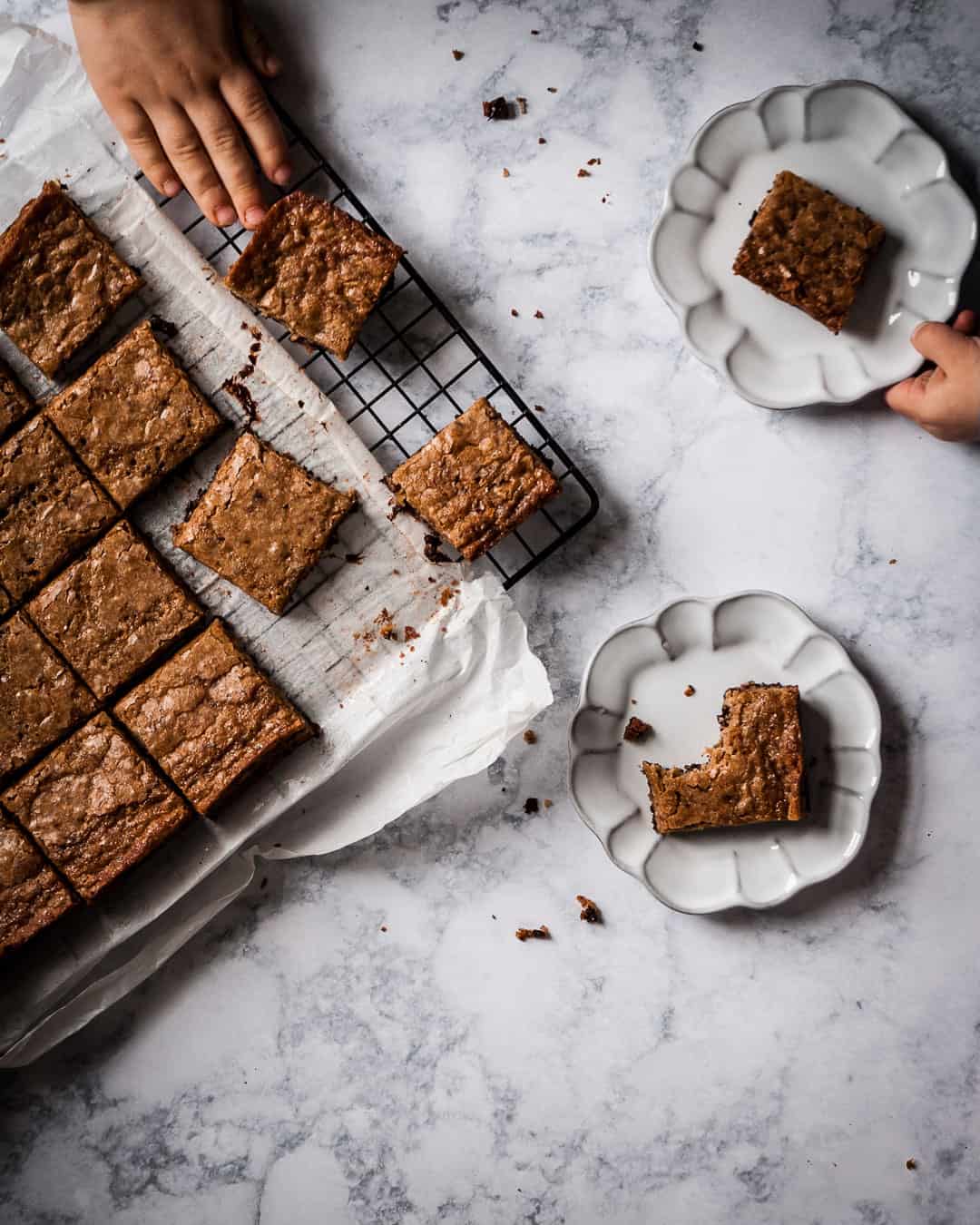 children's hands reaching for butterscotch dark chocolate bar cookies on a rack and plate