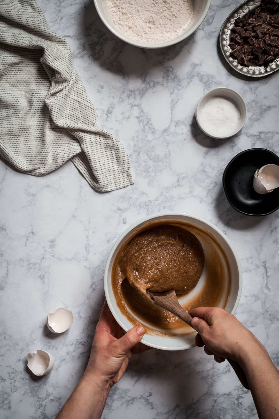 hands holding a spoon and stirring a bowl of butterscotch dark chocolate blondie bar cookie batter; kitchen process