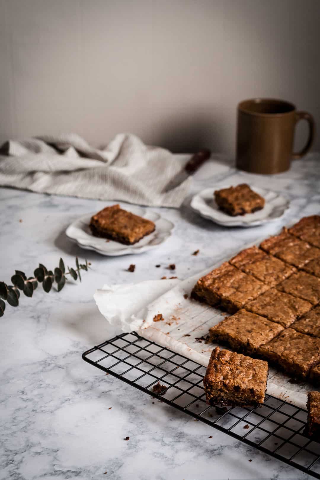 kitchen scene of butterscotch dark chocolate bars cooling on a marble counter with a knife and mug of coffee nearby