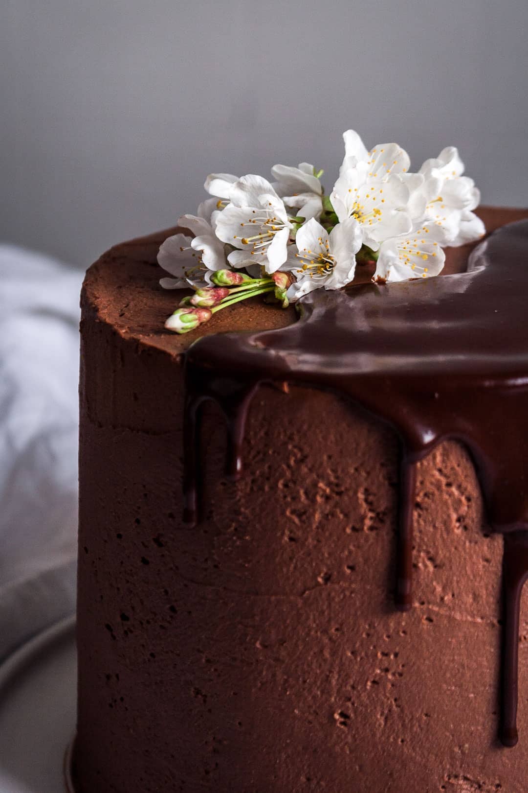 close up of marzipan cake with dark chocolate buttercream with ganache drip and cherry blossom decoration on top of cake