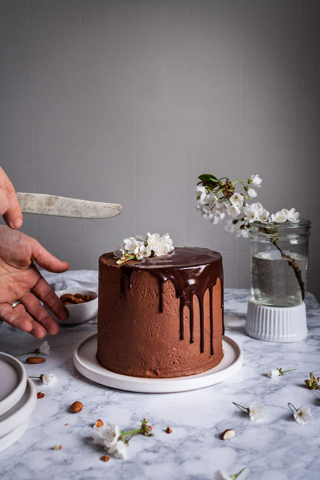 hands holding a knife and reaching out towards marzipan cake with dark chocolate buttercream sitting on a marble surface