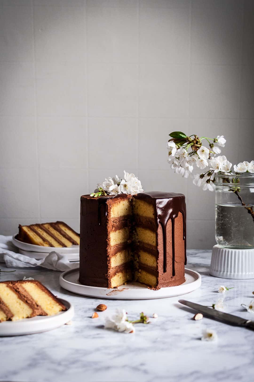 Marzipan and dark chocolate layer cake on white platter and marble background with cherry blossom garnish on the cake