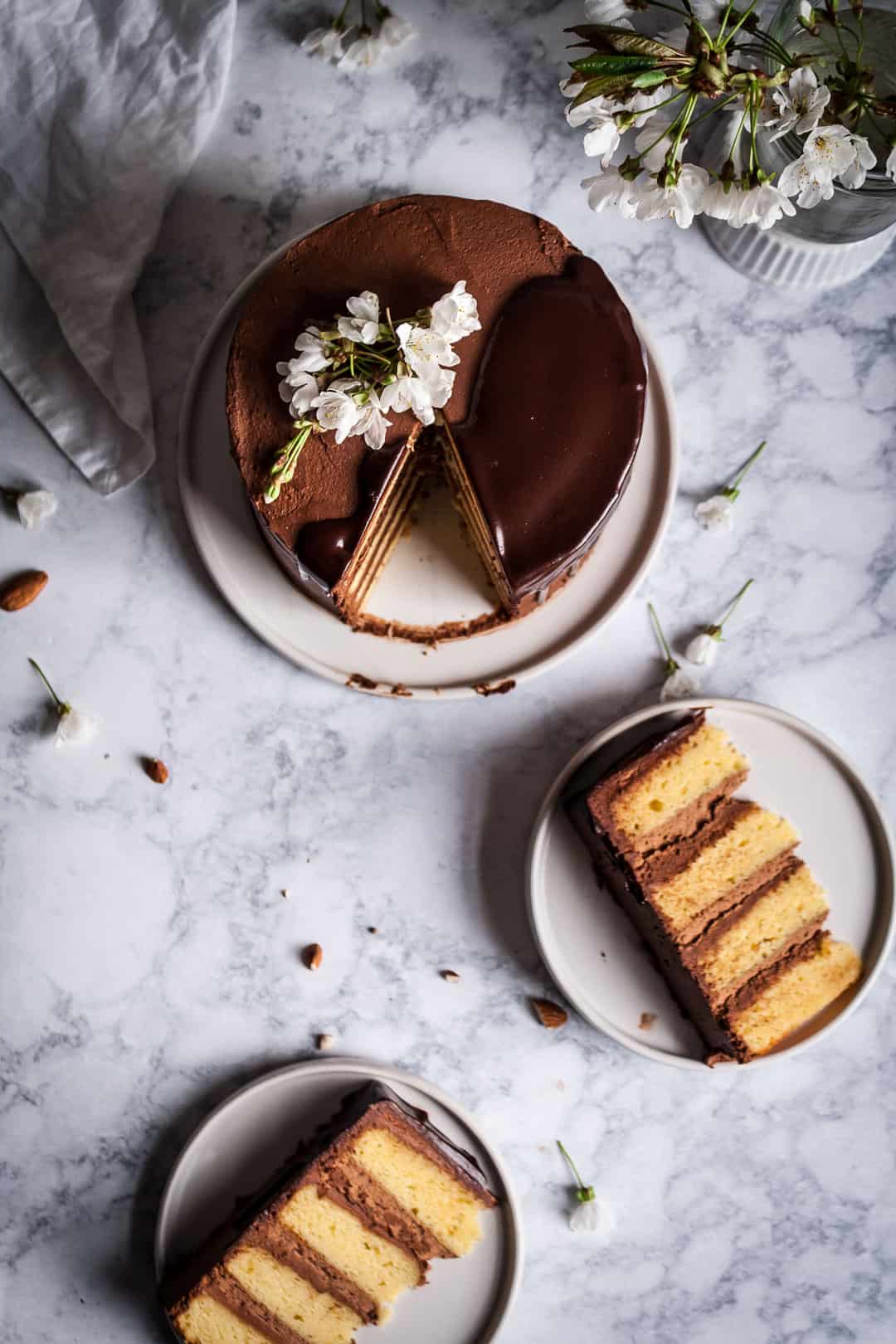 top view of marzipan cake with dark chocolate buttercream with two slices cut out and plated next to the cake on a marble surface