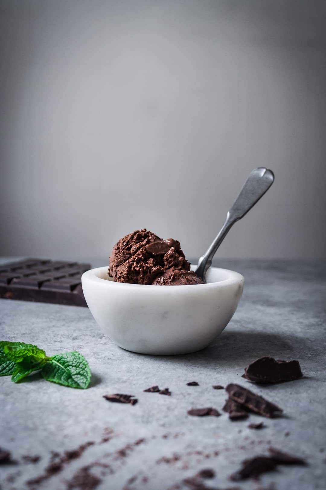 front view of small white bowl with a scoop of mint mocha chocolate chip ice cream and a spoon sticking up