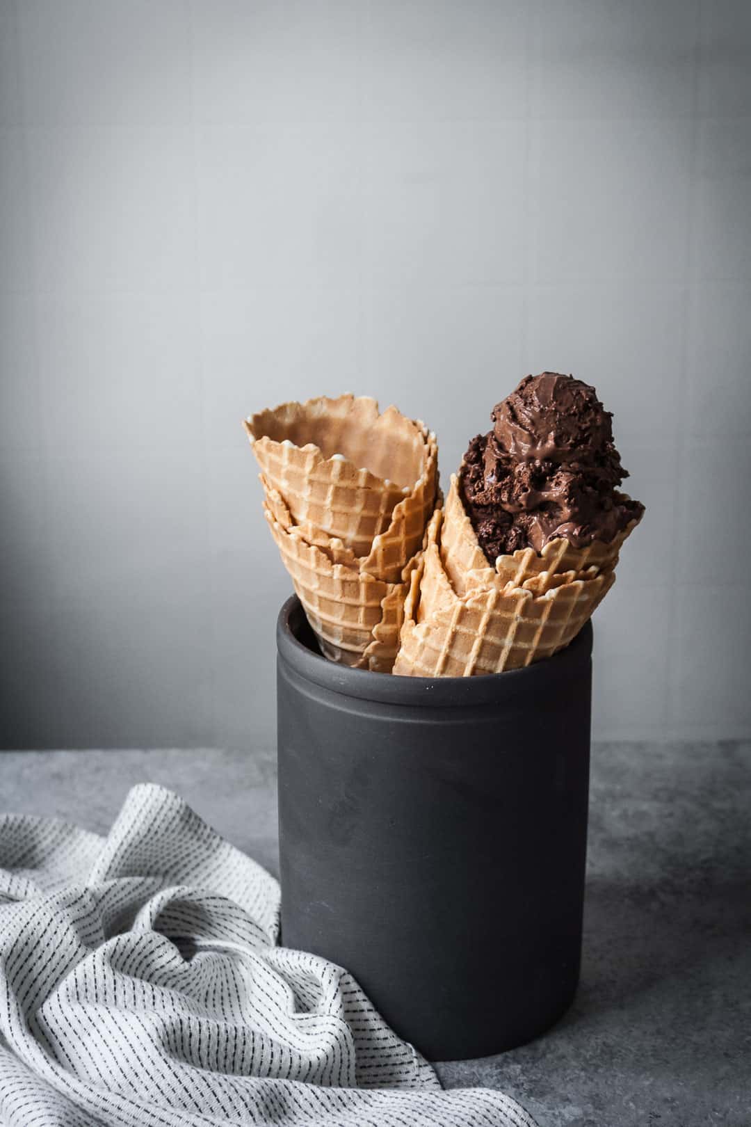 waffle cones in a black ceramic container on a table with a white kitchen cloth nearby