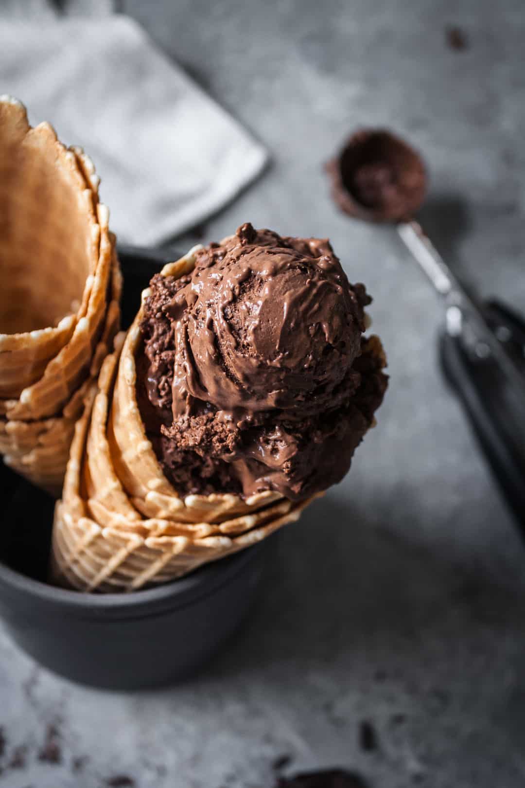 close up of scoop of mint mocha chocolate chip ice cream in a waffle cone with the ice cream scoop out of focus in the background