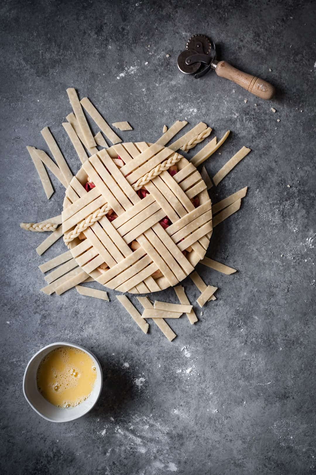 rhubarb apple pie with ginger and lemongrass on a grey surface with lattice top and extra dough trimmings lying near the pie tin