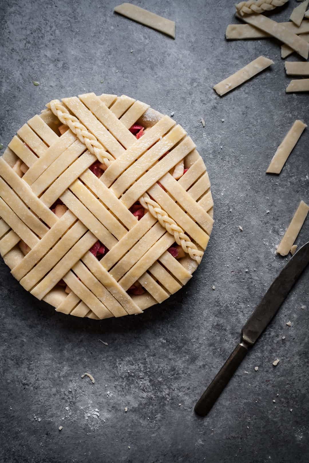 close up on a grey surface of rhubarb apple pie with ginger and lemongrass with lattice top including a small braid of dough