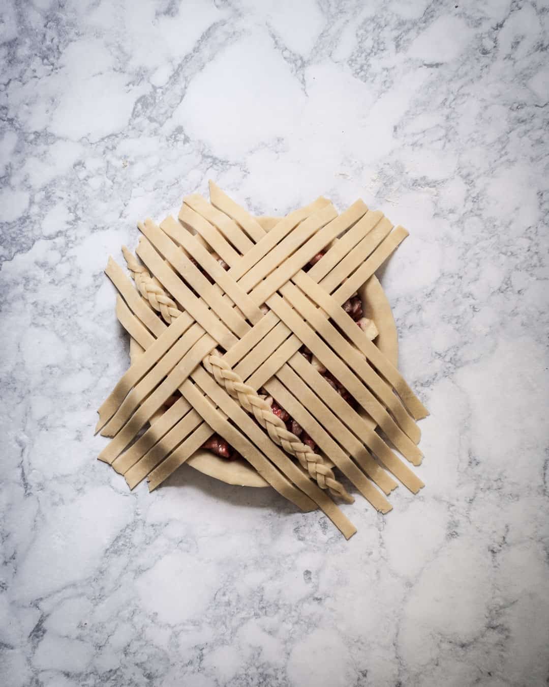 Process photo showing the fifth layer of lattice pie dough strips being covered by a layer from underneath.