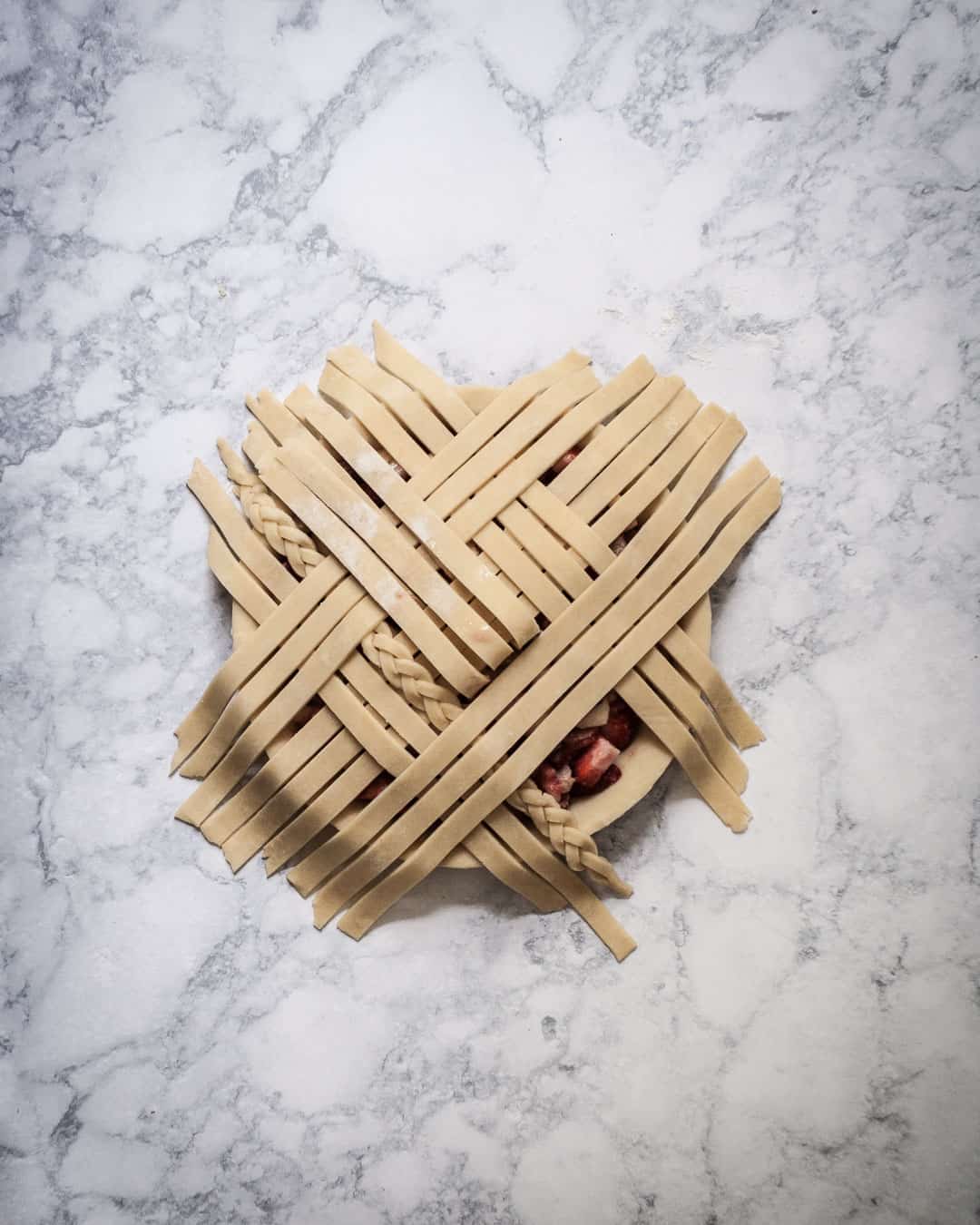 Process photo of another layer of lattice dough strips being added to a filled pie.