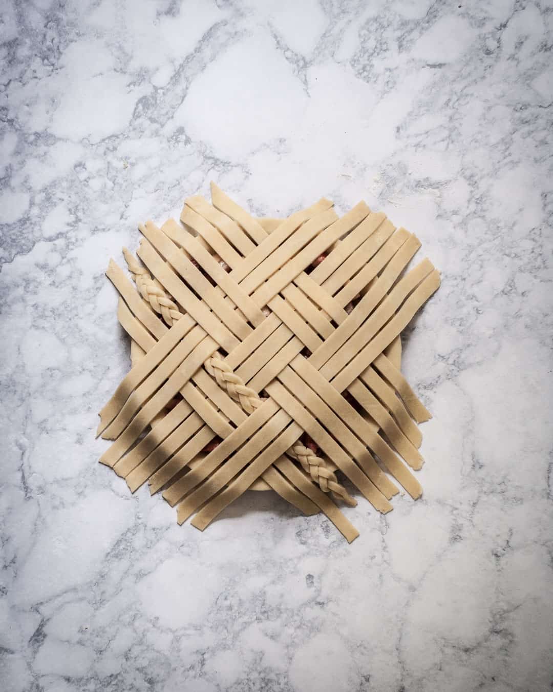 Process photo showing the last layer of lattice strips being folded back down onto the pie.