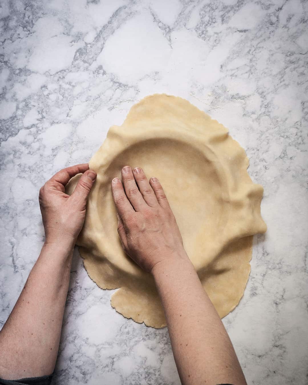 Hands pressing pie dough into a pan.