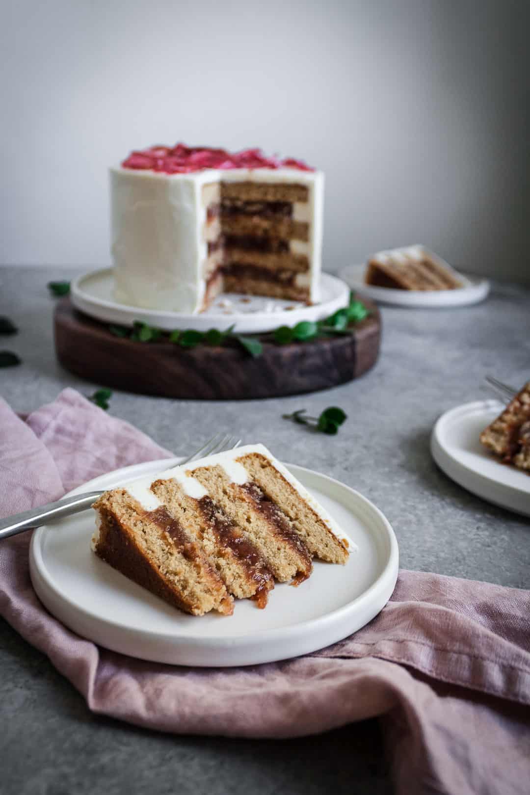 Slice of brown sugar cake with rhubarb compote and creme fraiche buttercream on a plate with the remainder of the cake in the background