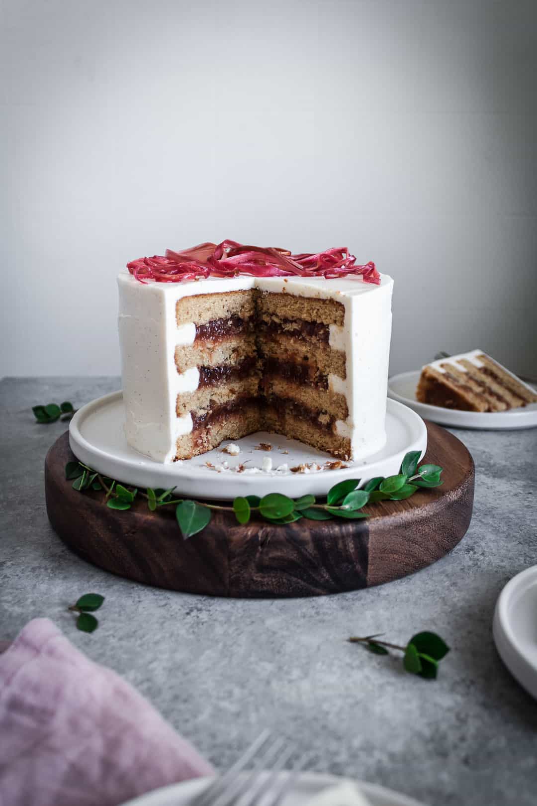 Side view of brown sugar cake with rhubarb compote and creme fraiche buttercream on a grey background