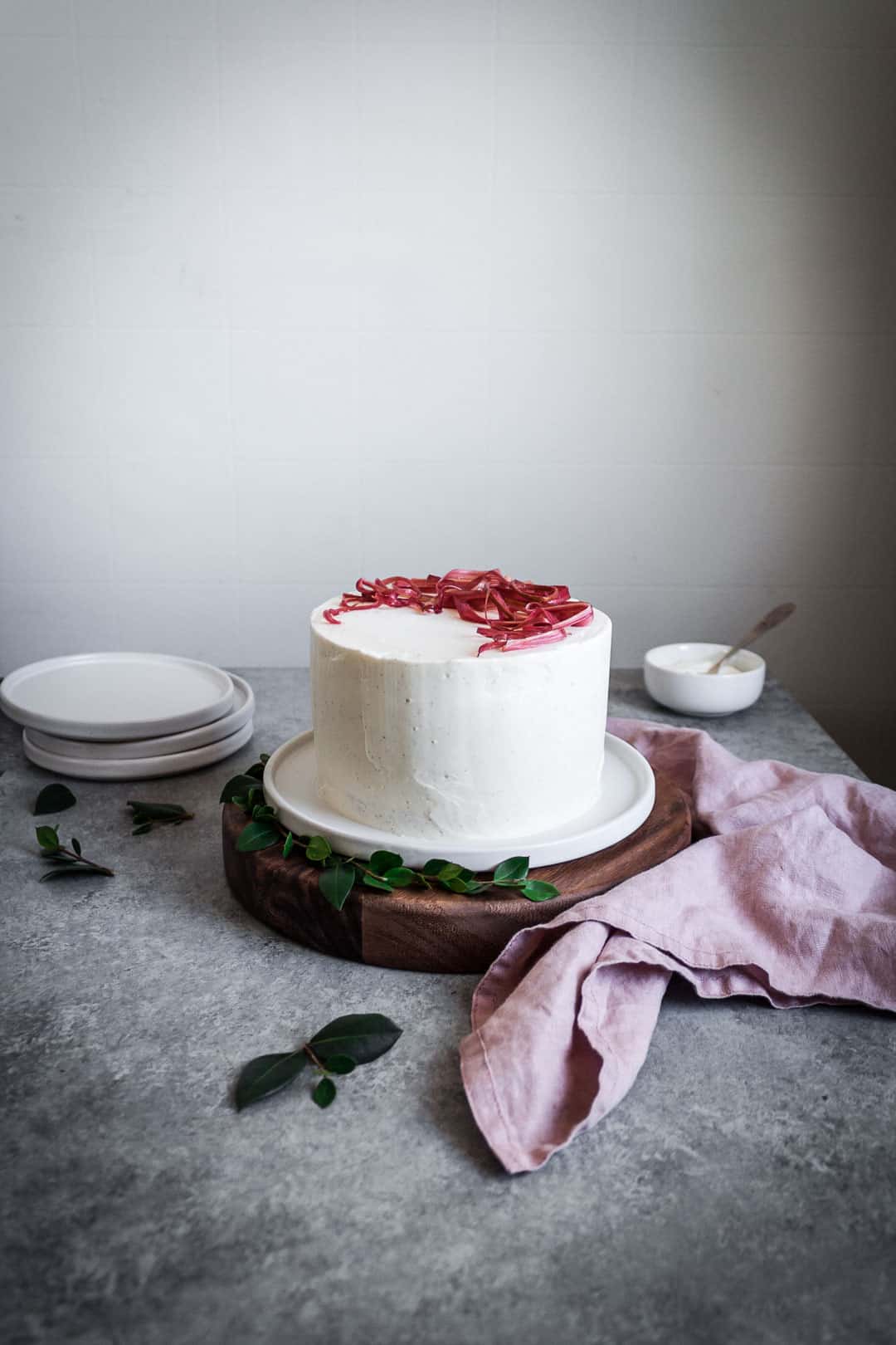 Side view of brown sugar cake with rhubarb compote and creme fraiche buttercream on a wooden platter with plates and napkin in foreground