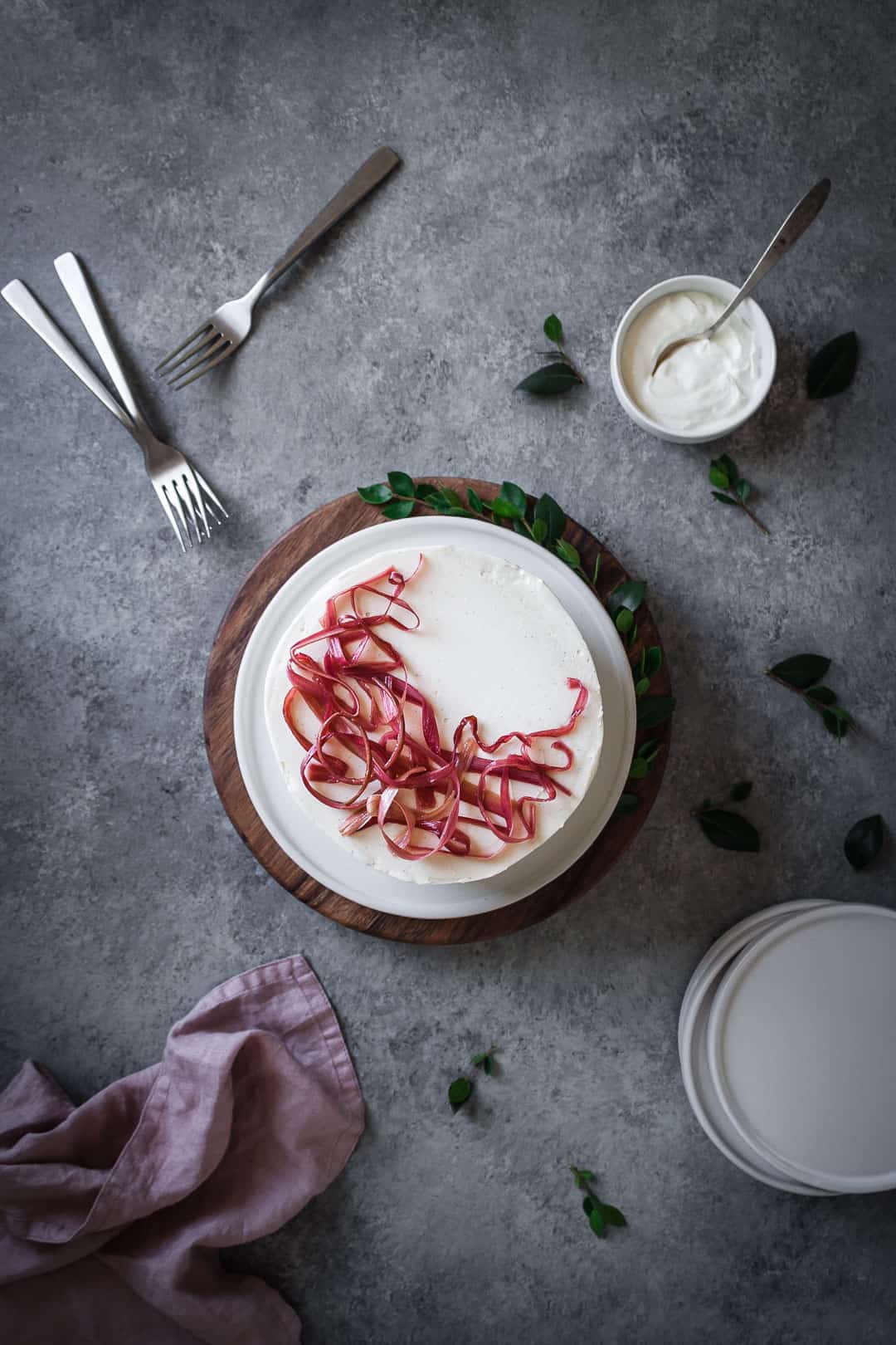 Top view of brown sugar cake with rhubarb compote and creme fraiche buttercream - table scene with forks, plates, napkin and pot of creme fraiche