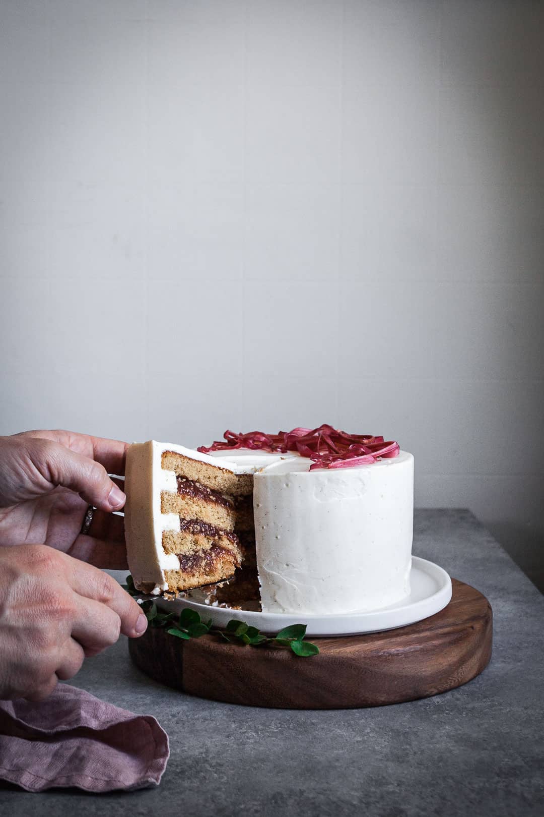 Side view of brown sugar cake with rhubarb compote and creme fraiche buttercream being cut with a knife with two hands in view