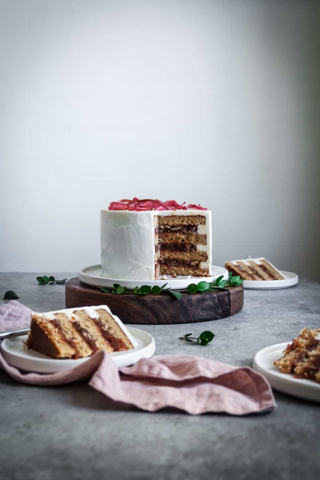 Three slices of brown sugar cake with rhubarb compote and creme fraiche buttercream on plates around the main cake