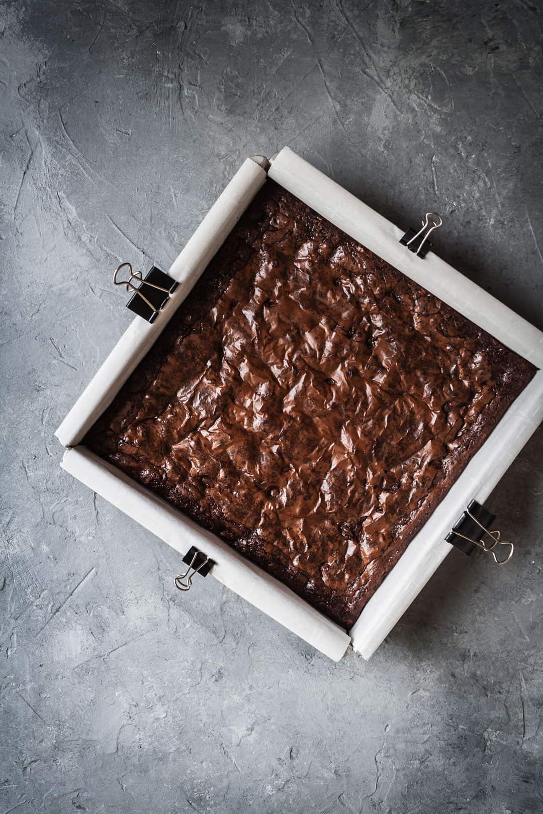 Overhead view of a square pan of brownies with port soaked cherries on a grey background