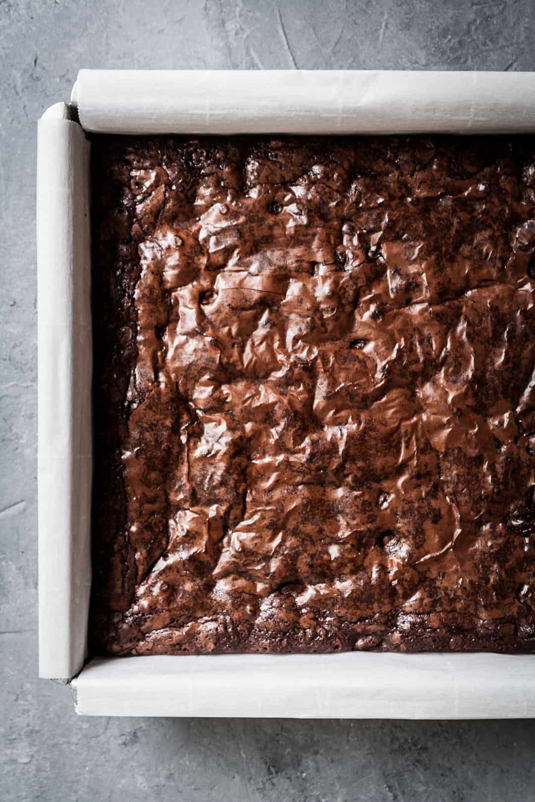 Close up overhead shot of brownies with port soaked cherries in a pan with crackly top on a grey background