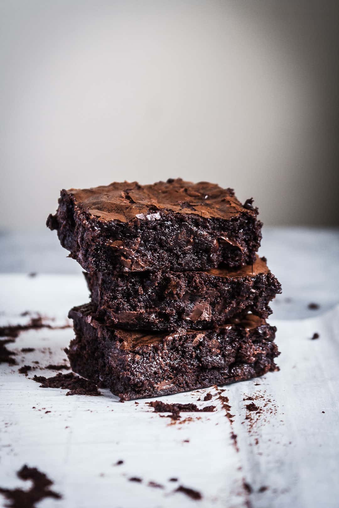 Side view close up of three squares of brownies with port soaked cherries stacked in a tower on parchment paper and a grey background