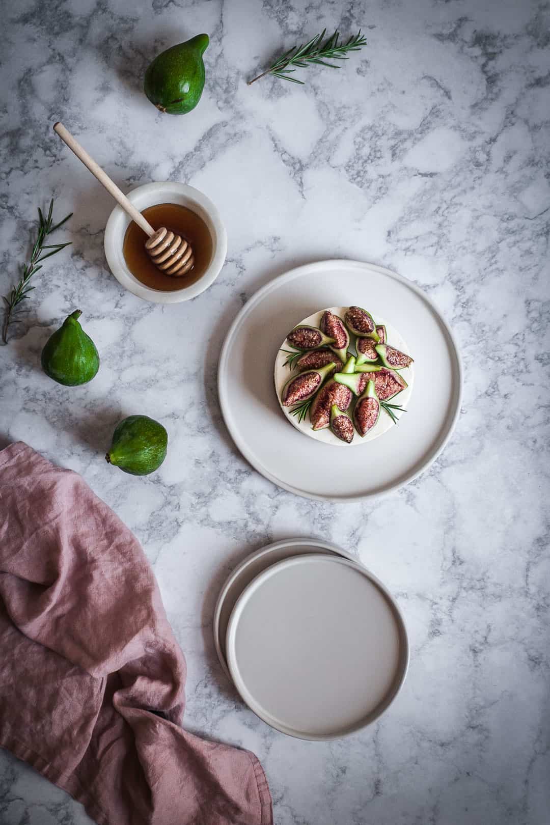 Honey orange cheesecake with figs and rosemary almond crust on a marble backdrop - birds eye view with white plates, green figs and a bowl of honey