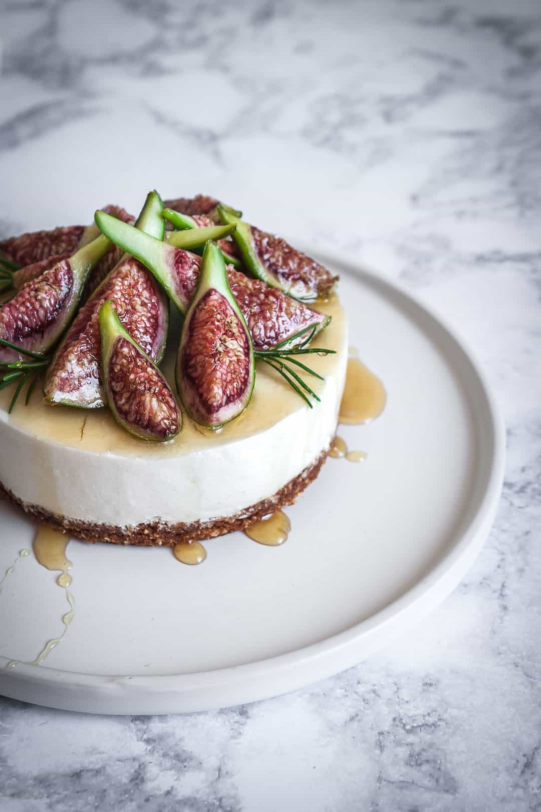 Honey orange cheesecake with figs and rosemary almond crust on a marble backdrop - angled close up view of cheescake with honey drizzled on top