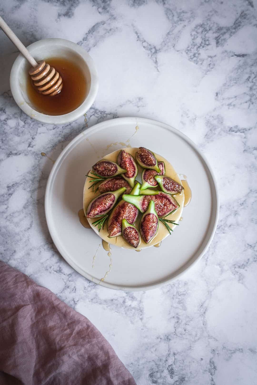 Honey orange cheesecake with figs and rosemary almond crust on a marble backdrop - birds eye view with white plate and a bowl of honey