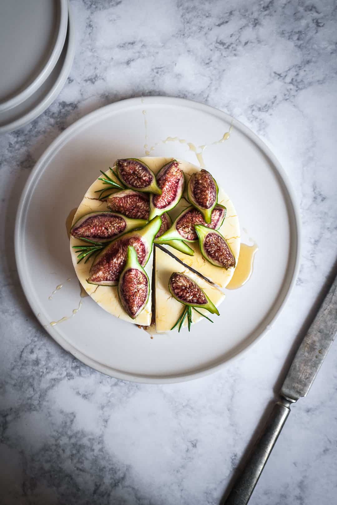 Honey orange cheesecake with figs and rosemary almond crust on a marble backdrop - birds eye view with slice cut and prepared on white plate with vintage knife nearby