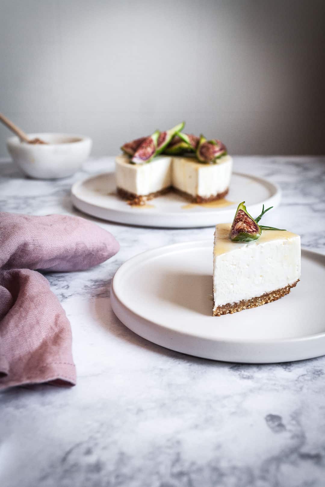 Honey orange cheesecake with figs and rosemary almond crust on a marble backdrop - birds eye view with white plates, pink linen napkin and a bowl of honey