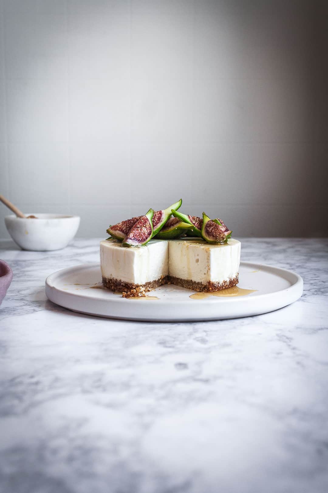 Honey orange cheesecake with figs and rosemary almond crust on a marble backdrop - side view with white plate and slice missing