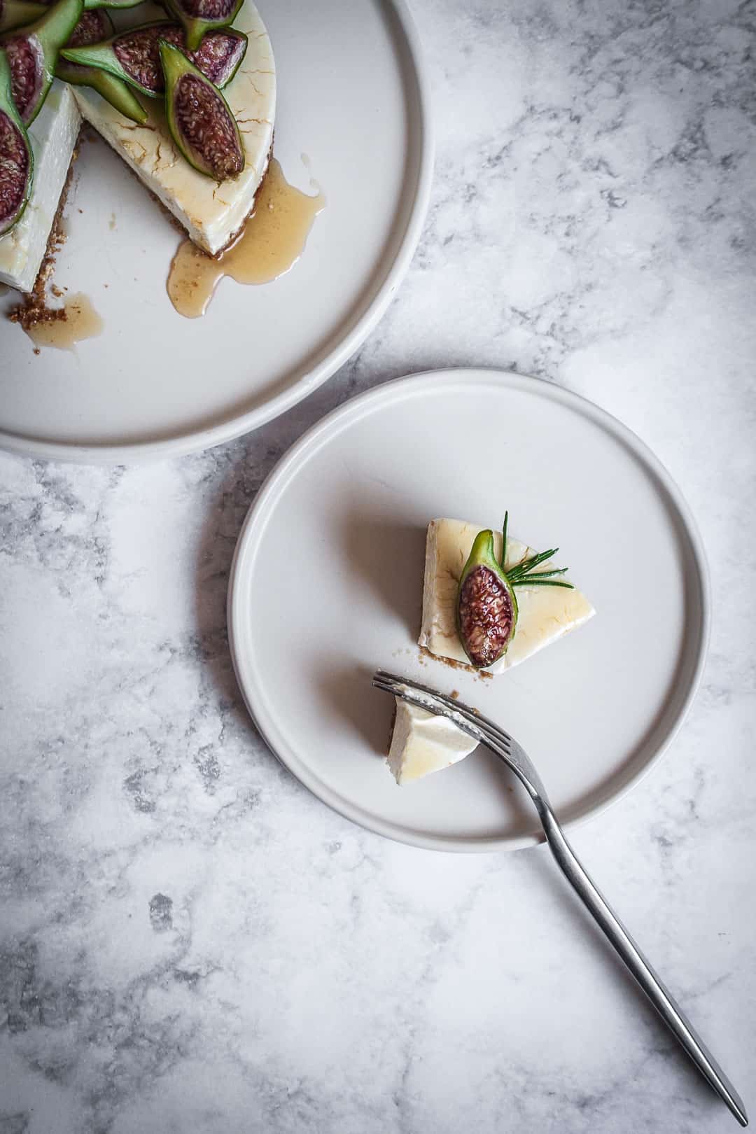 Honey orange cheesecake with figs and rosemary almond crust on a marble backdrop - birds eye view with slice of cheesecake on white plate 