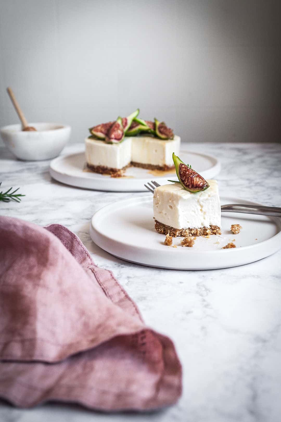 Honey orange cheesecake with figs and rosemary almond crust on a marble backdrop - side view with white plate and slice cut out