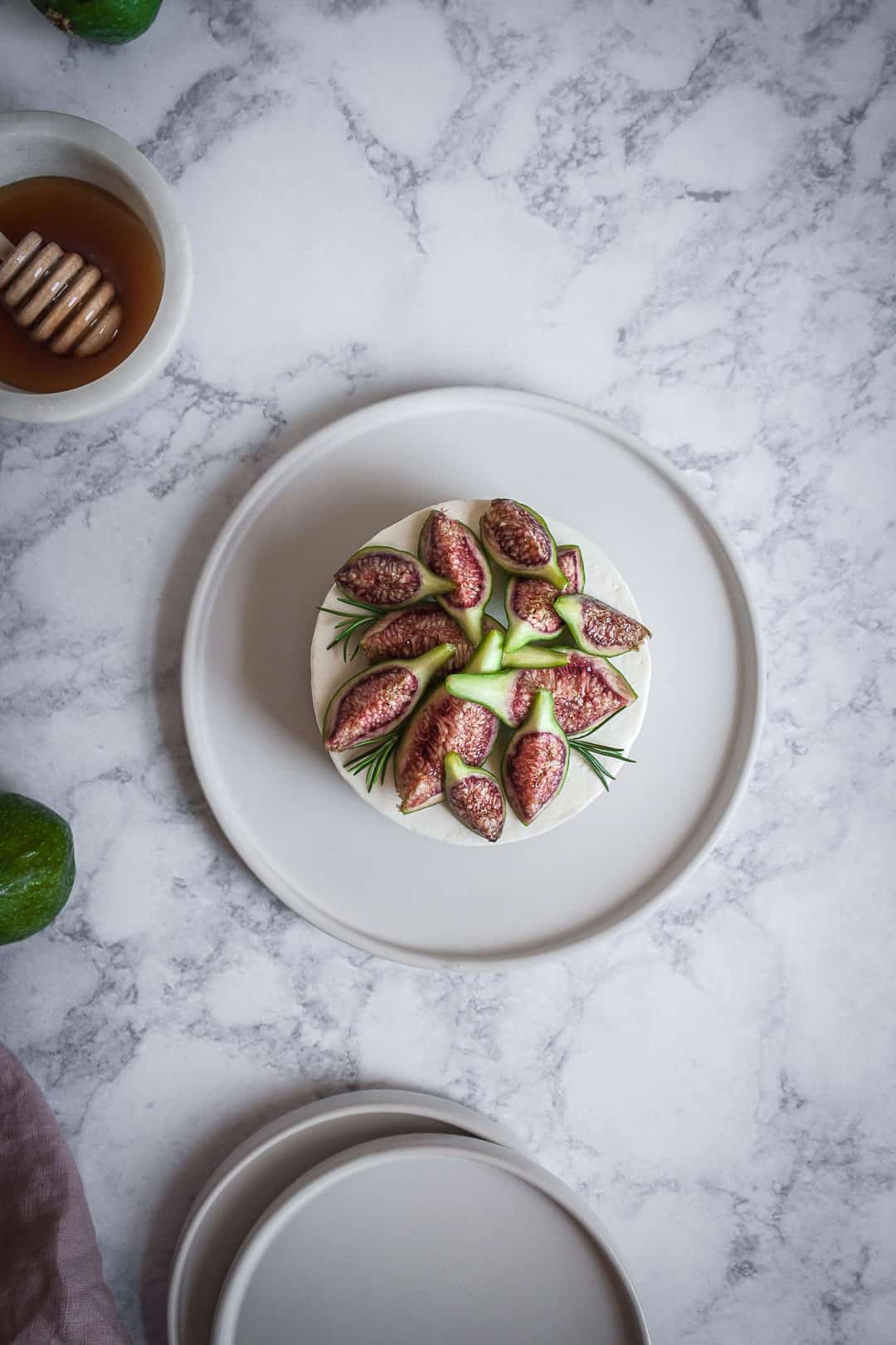 Honey orange cheesecake with figs and rosemary almond crust on a marble backdrop - birds eye view with white plate, green figs and a bowl of honey