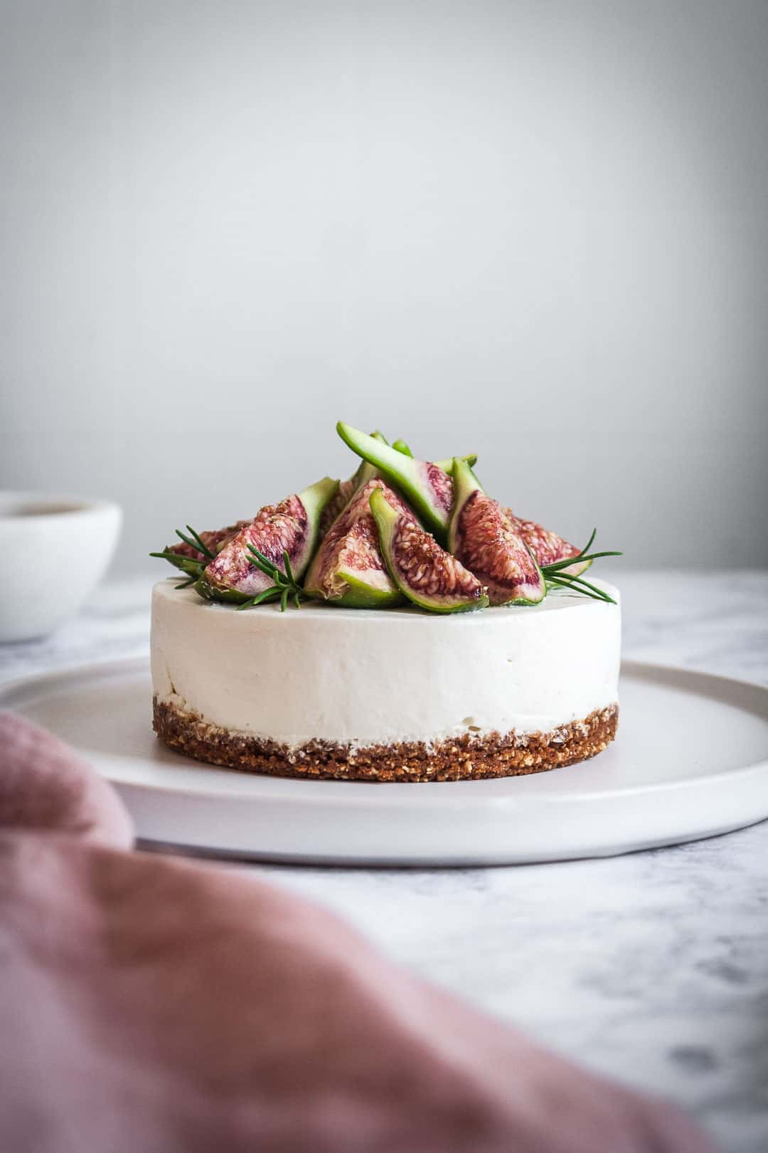 Honey orange cheesecake with figs and rosemary almond crust on a marble backdrop - side view of cheesecake with figs on top