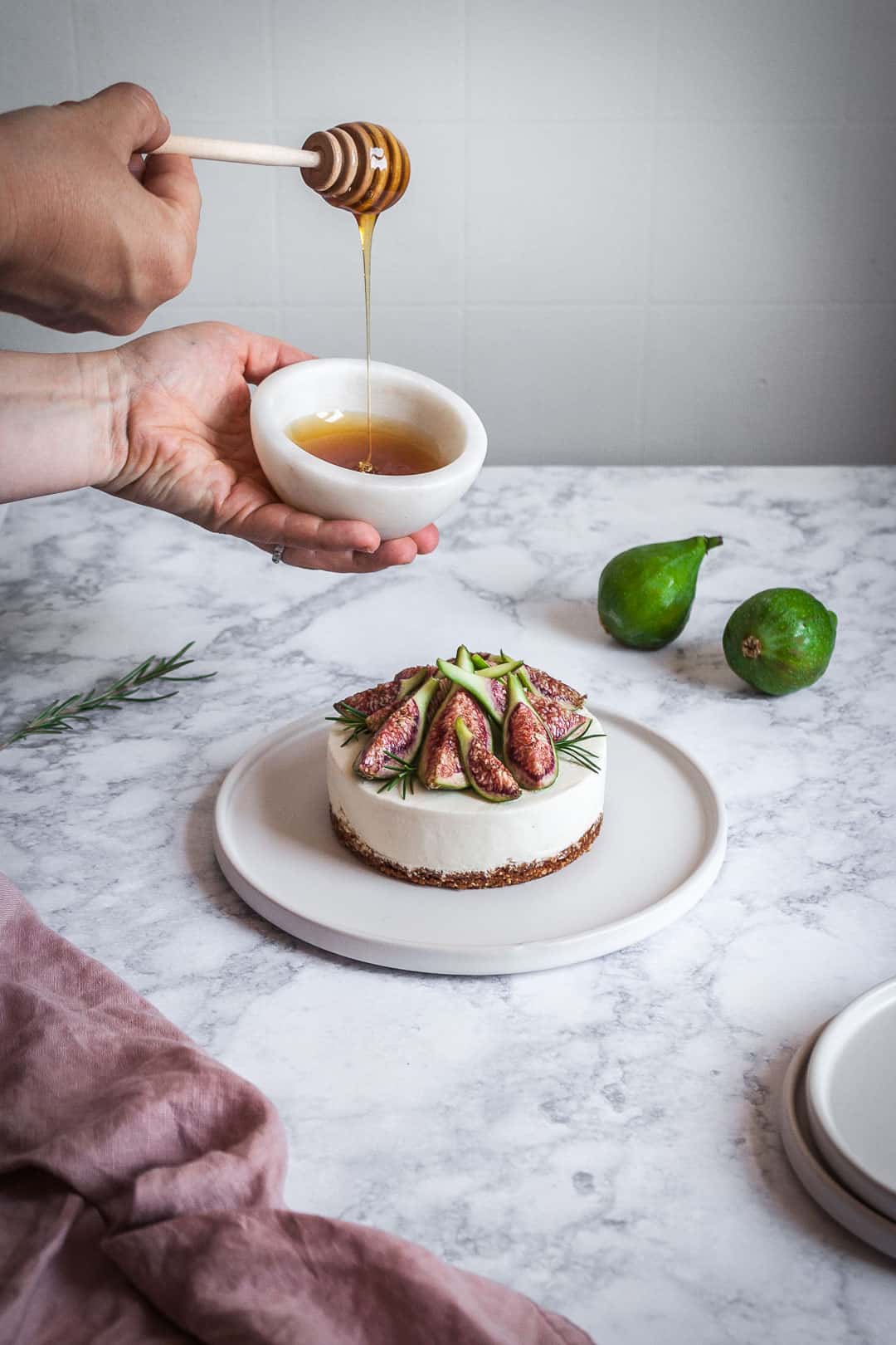 Honey orange cheesecake with figs and rosemary almond crust on a marble backdrop - birds eye view with white plates, green figs and a bowl of honey