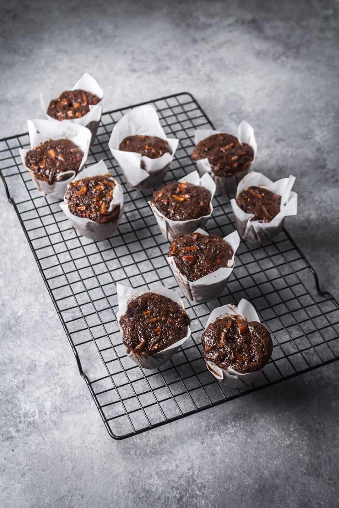 Apple mini cakes in parchment liners on a black cooling rack. The rack rests on a grey stone surface.