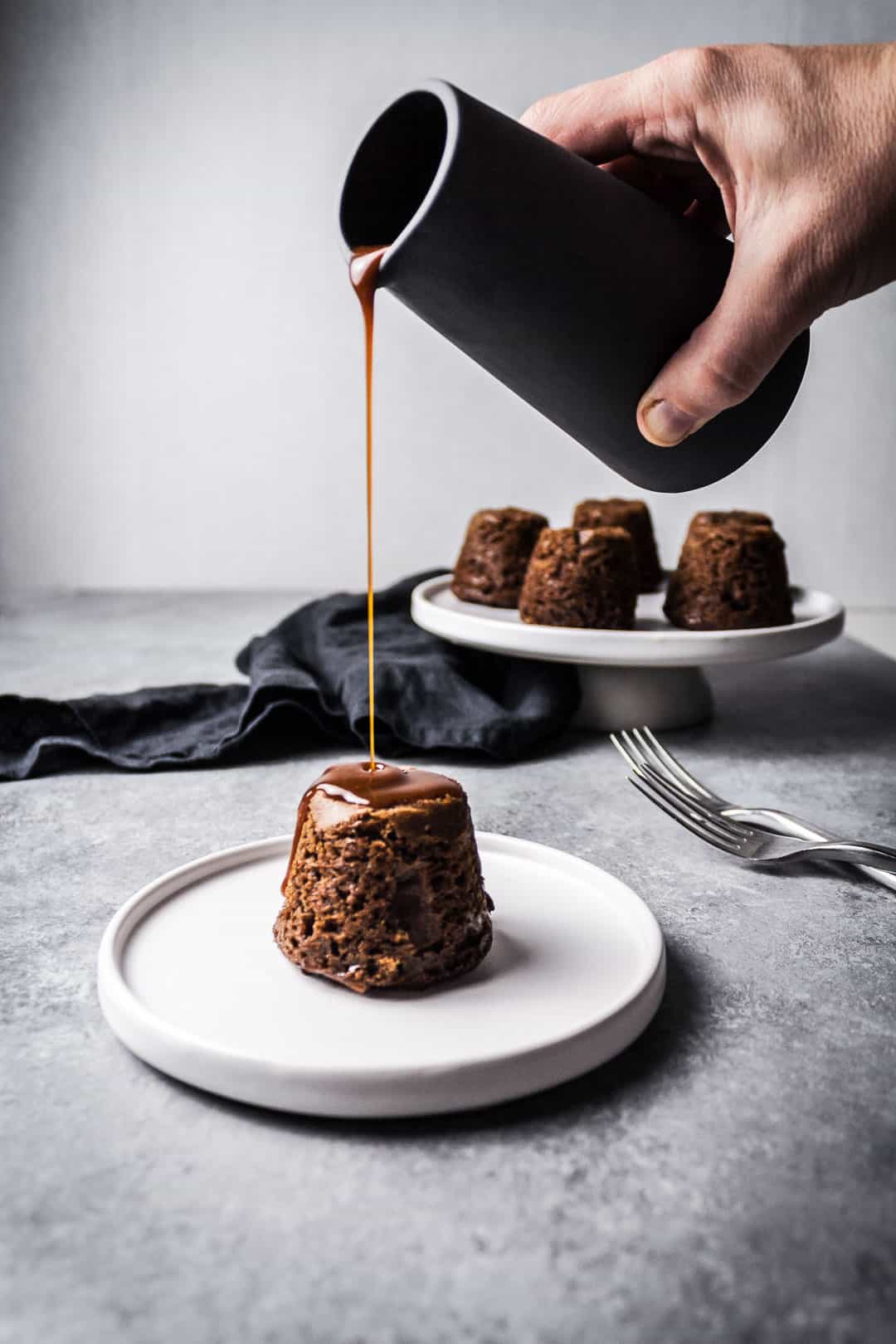 Front view of an apple ginger mini cake with a hand holding a ceramic pitcher pouring salted caramel sauce onto the cake