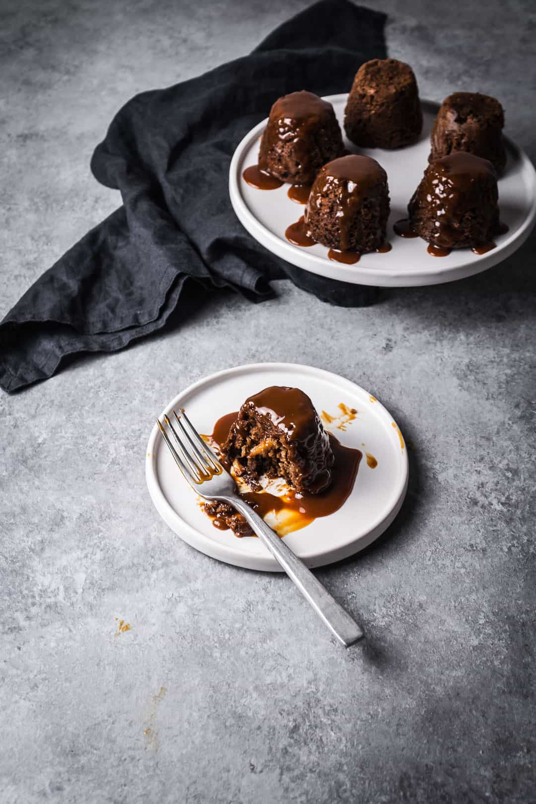 Closeup of an apple ginger mini cake on a plate with caramel sauce on top - partially eaten, with more cakes in the background