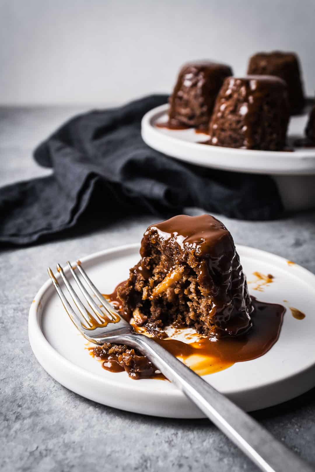 Closeup of an apple ginger mini cake on a plate with caramel sauce on top - partially eaten, with more cakes in the background