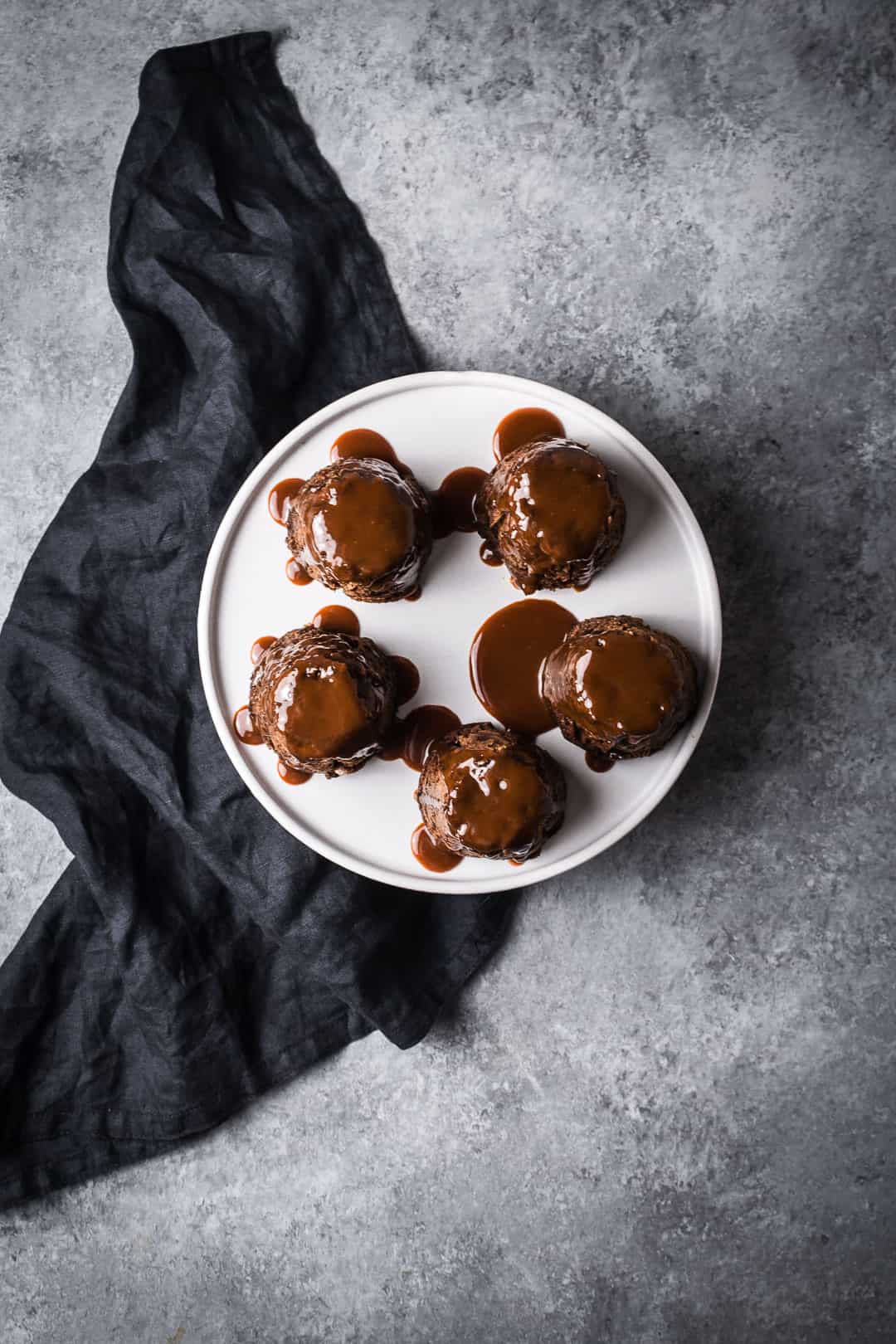 Top view of five apple ginger mini cakes topped with salted caramel sauce on a white plate with a grey background