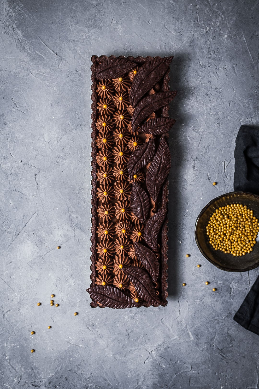 A rectangular salted caramel chocolate tart with chocolate tart dough leaves as decoration.