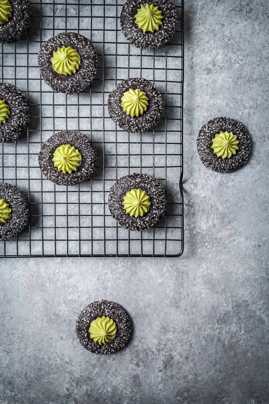 Top view of mint matcha chocolate thumbprint cookies on cookie rack with grey background