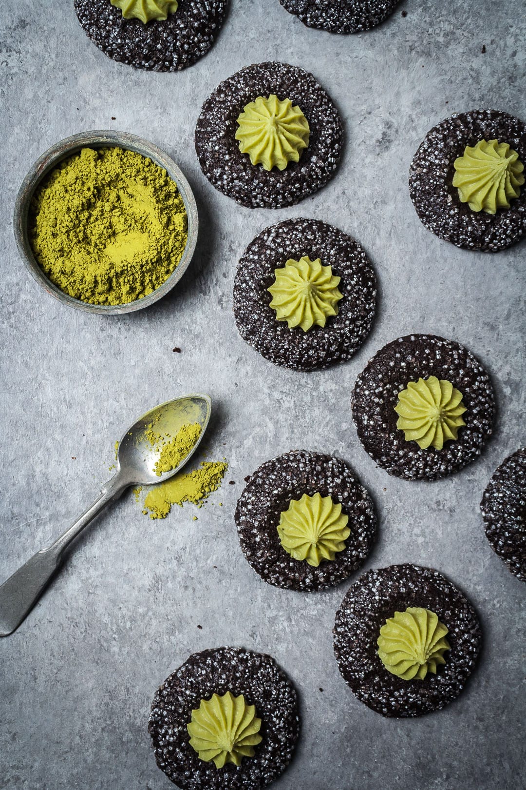 Top view of Mint Matcha Chocolate Thumbprint Cookies on a grey background with container of matcha and spoon nearby