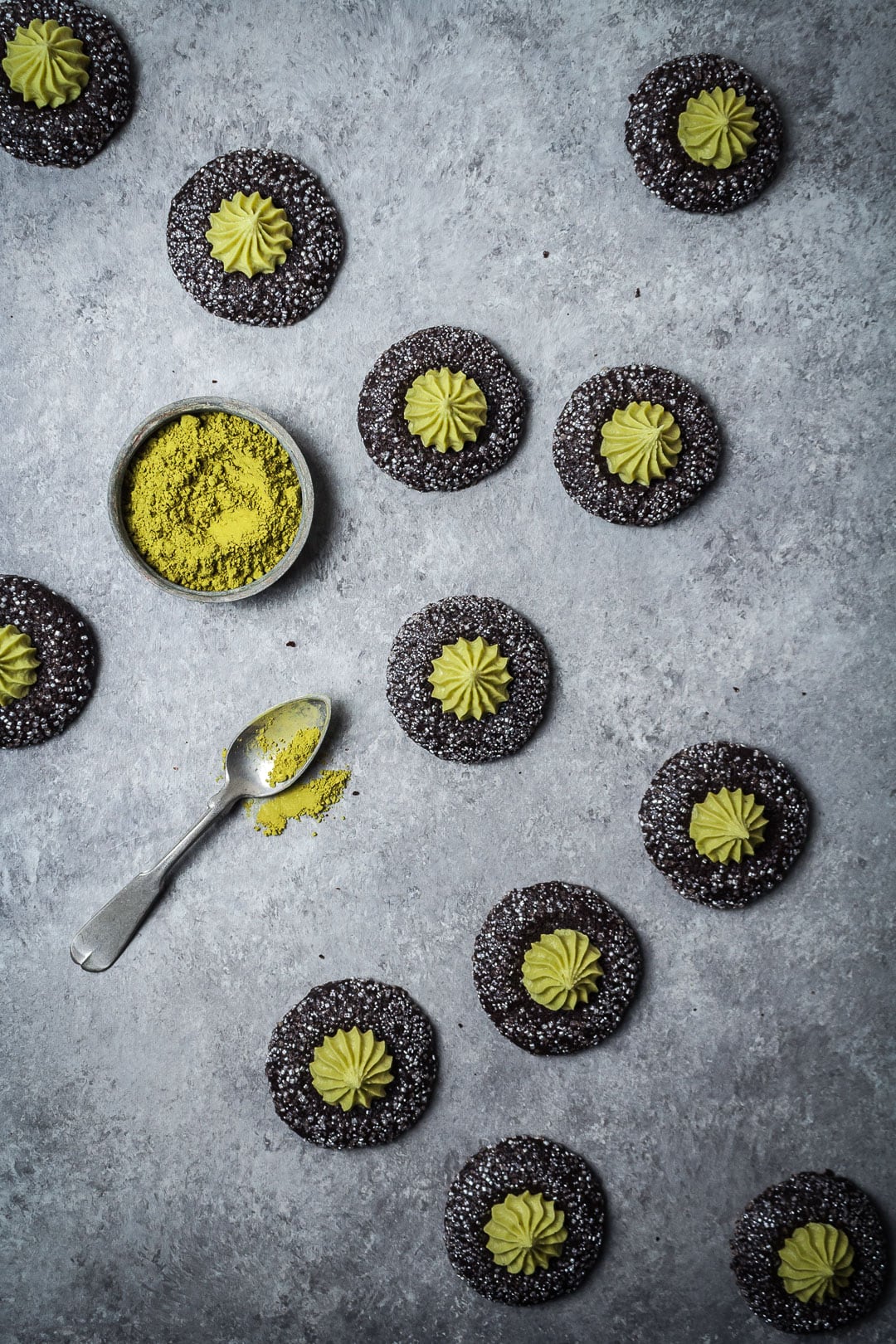 Top view of Mint Matcha Chocolate Thumbprint Cookies on a grey background with container of matcha and spoon nearby