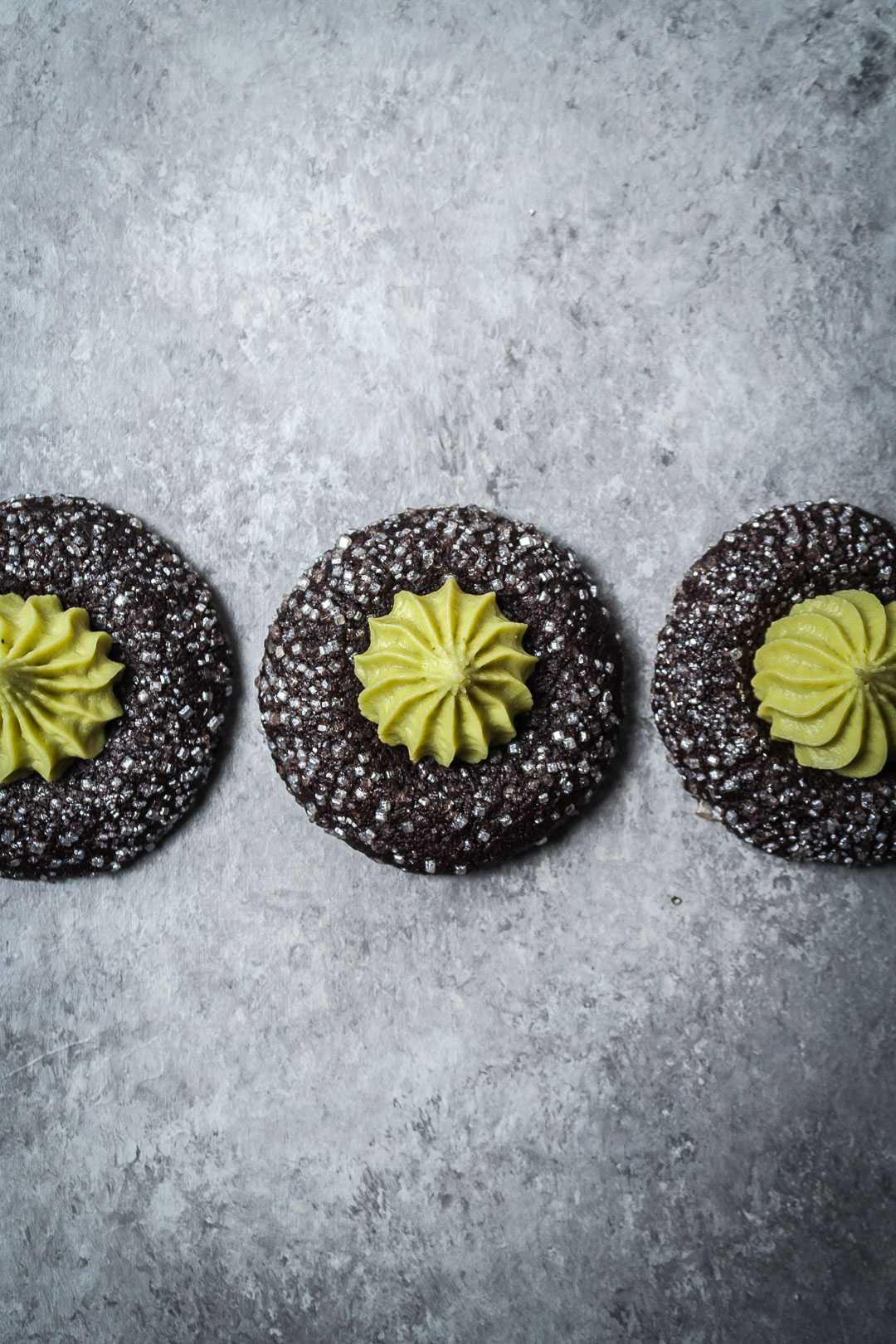 Top view of three mint matcha chocolate thumbprint cookies in a row on a grey background