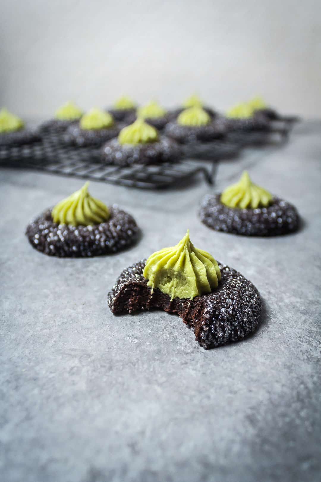 Side view of mint matcha chocolate thumbprint cookies with a bite taken out of one, resting on grey background