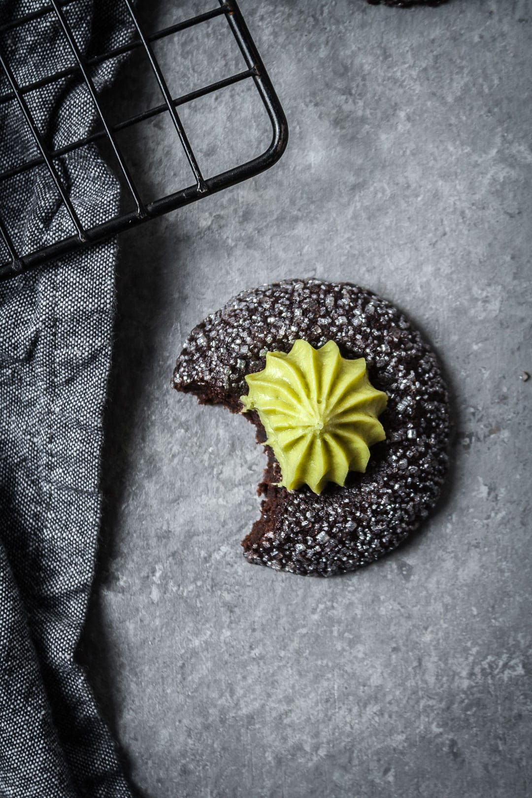 Close up of mint matcha chocolate thumbprint cookie with bite taken out on a grey background