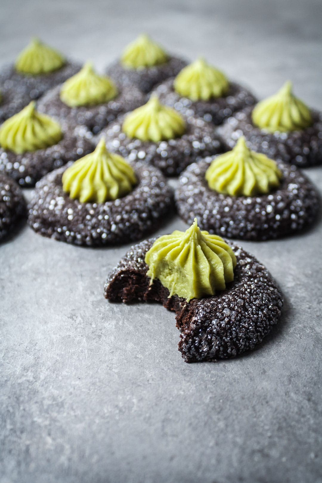 Side view of mint mocha chocolate thumbprint cookies on a grey background with bite taken out of one