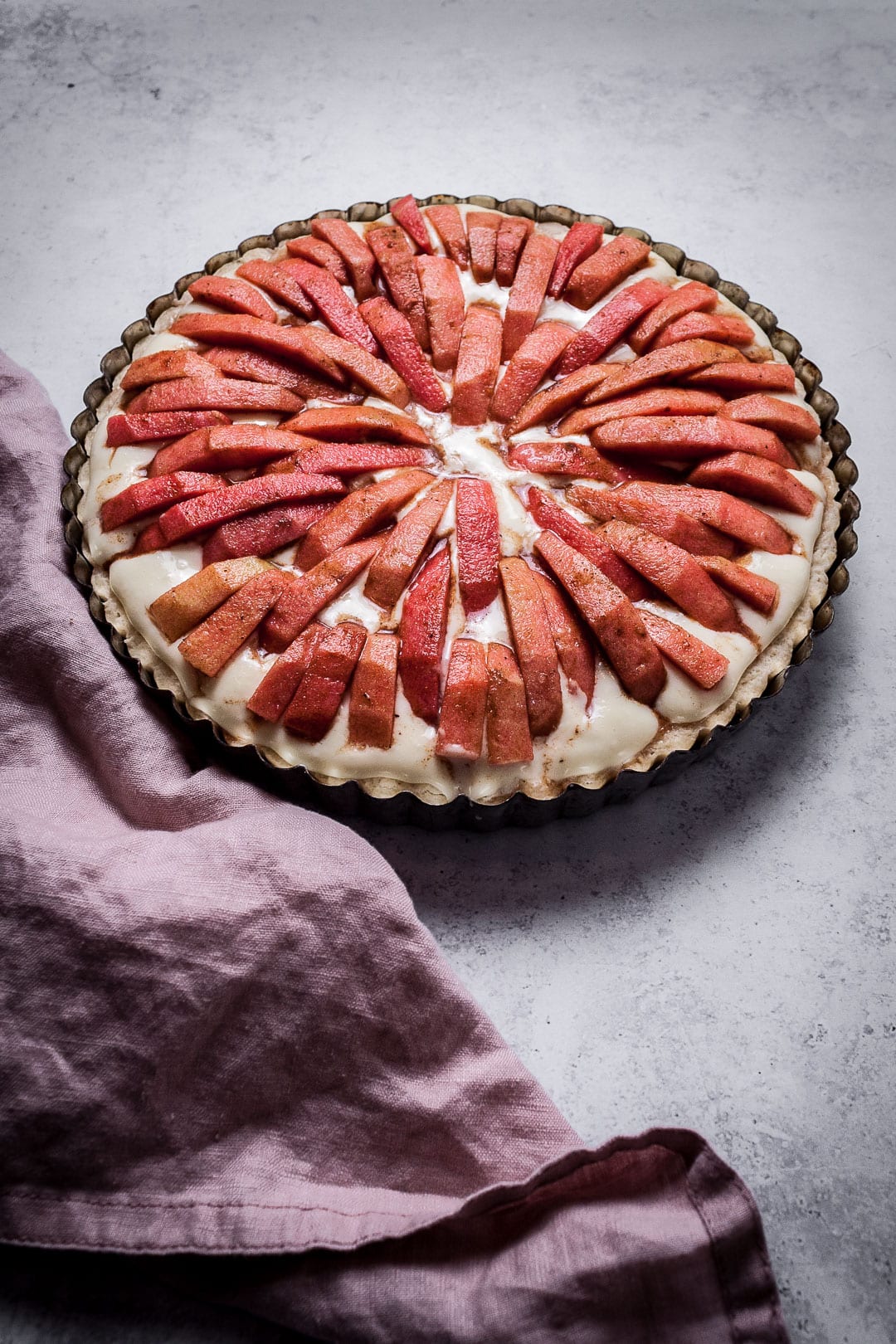 Pink Apple Tart with Cream Cheese Filling on a grey background with pink napkin - prior to baking